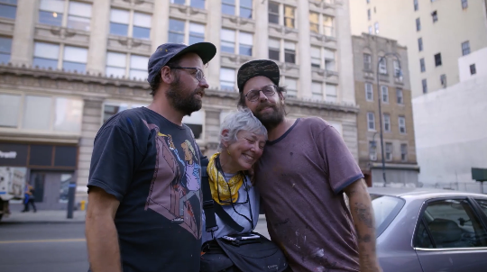 Brisbane-based colourist Angela Cerasi from Peachy Keen Colour graded this shot of New York photographer Martha Cooper being embraced by two young men with caps, glasses and beards, for the documentary Martha: A Picture Story