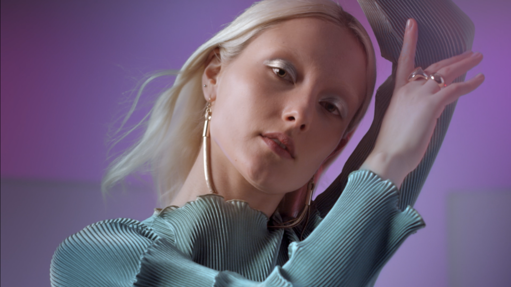 Peachy Keen Colourist Angela Cerasi colour graded this medium close up shot of a white, blond model with blue eyeshadow and a blue silk dress, posing in a purple-lit room, for the Afterpay Australian Fashion Week TVC campaign for LG X Harvey Norman in this example of colour grading video