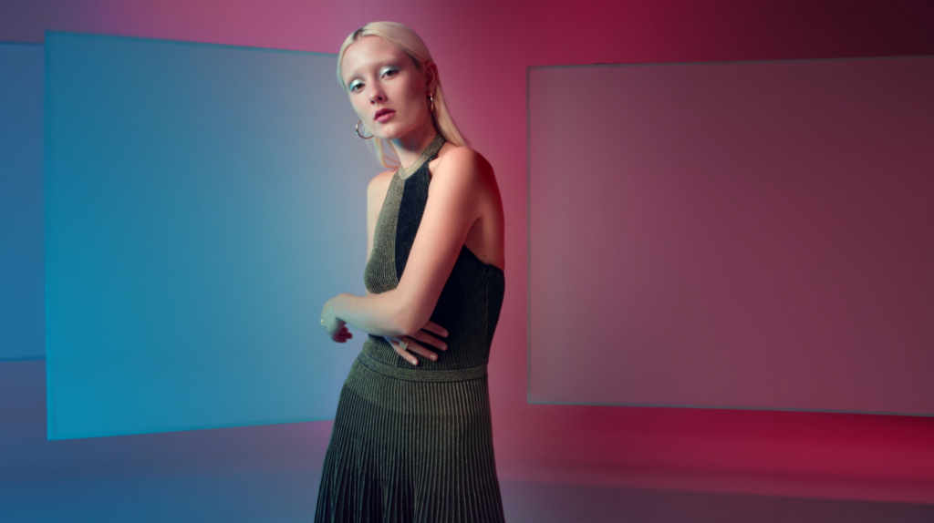 Peachy Keen Colourist Angela Cerasi colour graded this shot of a white, blond model with blue eyeshadow and a black and gold dress, posing in a pink and blue-lit room, for the Afterpay Australian Fashion Week TVC campaign for LG X Harvey Norman